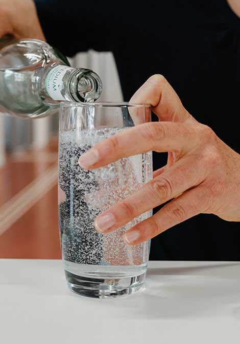 Ein Glas wird mit Hilfe der Einschenk-Technik mit Sprudelwasser gefüllt
